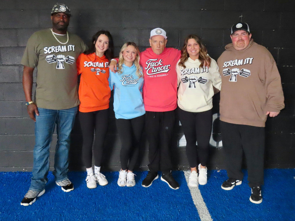 Six people standing together in front of a black brick wall and blue turf, wearing matching graphic apparel with 'SCREAM IT!' text and a skull-and-crossbones logo.